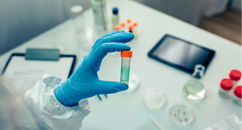 Scientist in a lab wearing blue gloves holding a small beaker with pale blue liquid inside