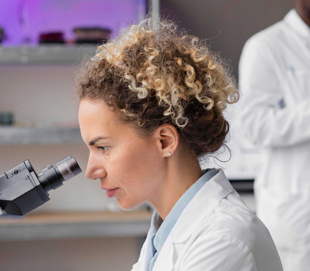 Scientist in a lea wearing a lab coat sat down looking through a telescope