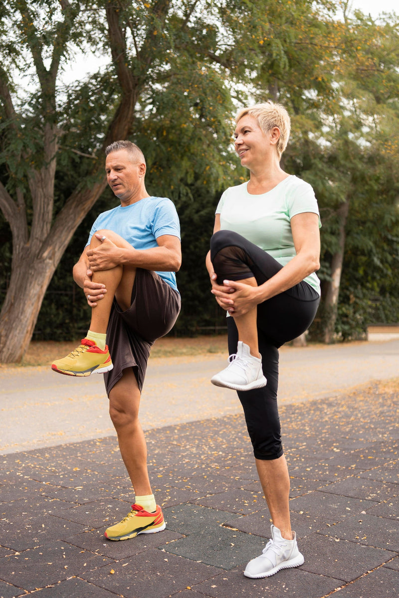 Couple exercising and lifting one leg up and holding the top their leg just beneath the knee